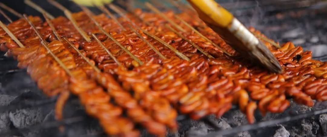 Skewers being basted with sauce over the charcoal grill